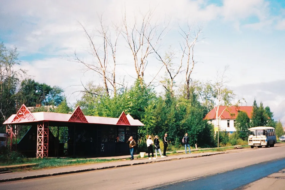 Quaint rural bus stop with people ready to catch a ride, surrounded by nature.