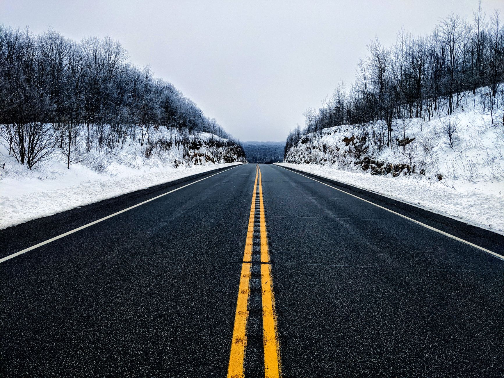 A quiet winter highway stretching through a snowy Pennsylvania forest. Perfect symmetry and seasonal beauty.