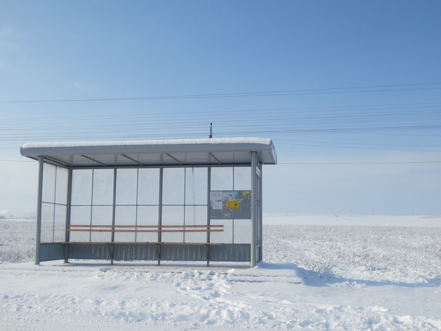 A solitary bus stop in a vast snowy field under a clear blue sky, offering tranquility.